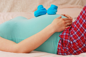 Pregnant woman lying with baby shoes on her stomach