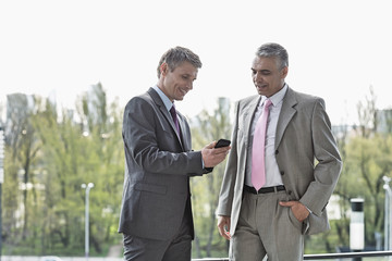 Businessmen using cell phone together outdoors