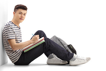 Teenage student leaning against a wall writing in a notebook