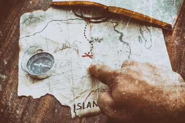 Man point by finger to red cross on vintage old fake pirate map of Treasures. Adventure time