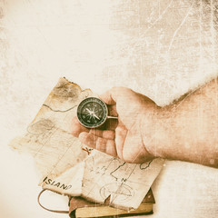 Man holds compass in front of fake treasure map with red cross and grunge and vignette effect
