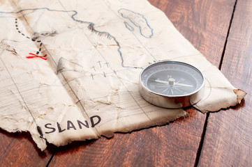 Close up to fake Pirates Treasure map with red cross and compass on wooden table background.