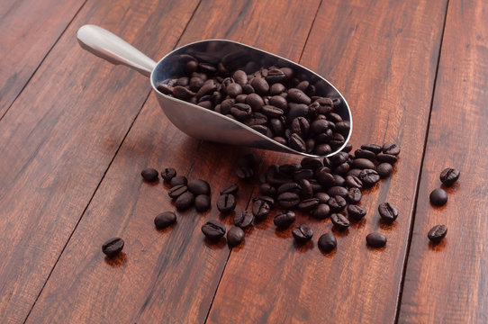 Fresh roasted black coffee bean on wooden desk with steel spoon