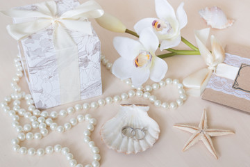 Fototapeta na wymiar Present, beads, seashells, orchid and rings on wooden background