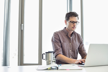 Businessman working on laptop at desk in creative office