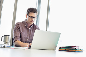 Mid-adult businessman working laptop at desk in creative office