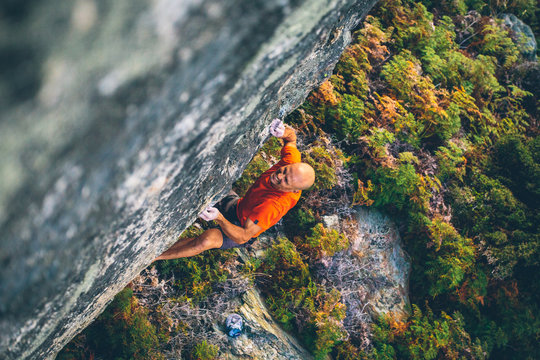 Rock climber with no ropes above green forest