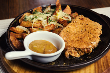 Pork steak with fried potatoes served in a frying pan served with mustard sauce. Serving dishes in a restaurant, European cuisine, European restaurant, pub