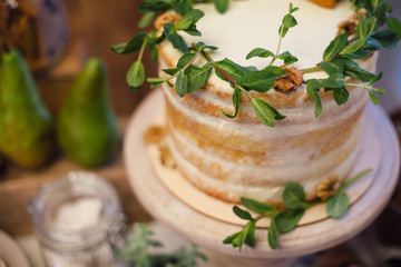 white wedding cake decorated with greenery, stands on a table in the banquet area.Candy-bar.Focus on greenery