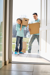 Fototapeta na wymiar Happy father and son with cardboard boxes entering into new house