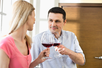Couple toasting red wine glasses in kitchen
