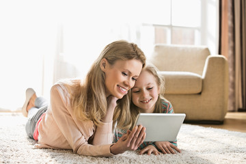 Mother and daughter using digital tablet on floor at home