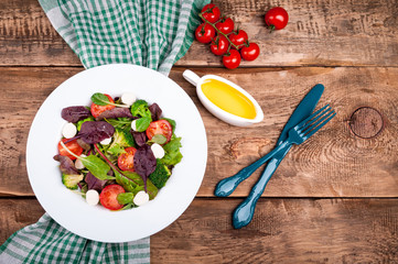 Fresh salad with spinach, arugula, broccoli, tomato, mozzarella cheese, chard leaves and olive oil on wooden background. Healthy food and diet concept. Vegetarian food. Copy space. Top view