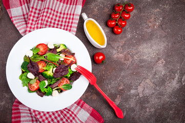 Fresh salad with spinach, arugula, broccoli, tomato, mozzarella cheese, chard leaves and olive oil on dark background. Healthy food and diet concept. Vegetarian food. Copy space. Top view