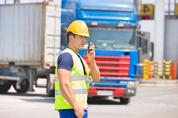 Mid adult man using walkie-talkie in shipping yard