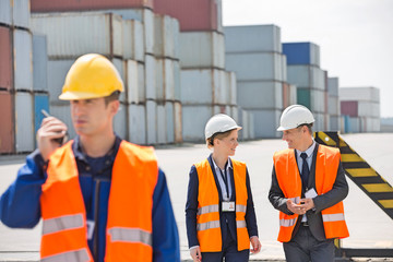 Worker using walkie-talkie while colleagues discussing in shipping yard