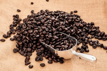 Heap of hot roasted coffee beans with metal spoon on brown burlap material
