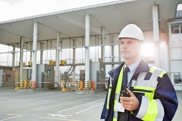 Middle-aged male worker holding walkie-talkie while looking away in shipping yard