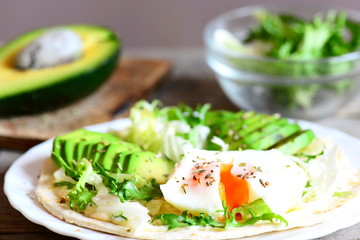 Healthy eating. Poached egg, avocado slices, cabbage, lettuce mix, tortilla, sauce and spices. Homemade egg and avocado tortilla on plate. Rustic style. Closeup