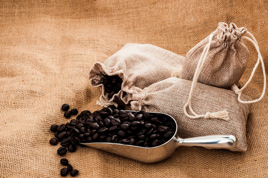 Steel spoon with heap of roasted coffee beans on burlap fabric surface
