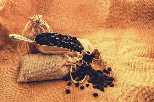 Heap of roasted coffee beans in steel spoon with sack on burlap surface with retro color effect