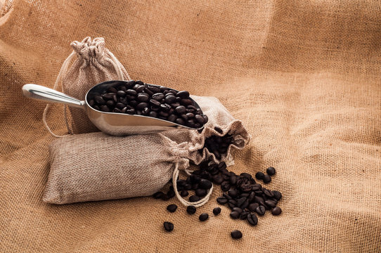 Steel spoon with heap of roasted coffee beans on old sack on burlap surface