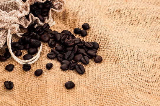 Heap of roasted coffee beans on crumpled burlap surface with old sack