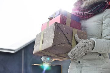 Midsection of woman carrying stacked gifts during winter by window