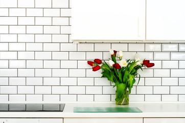 Fresh bouquet of red and white tulips on kitchen table. Detail of home interior, design. Minimalistic concept. Flowers for mother, girl, wife, woman. Copy space.