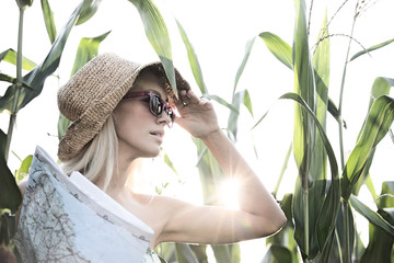 Woman looking away while holding map amidst plants on sunny day