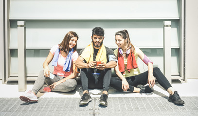 Fototapeta premium Happy friends having a break during sport fitness training using mobile smart phone - Young sporty people sharing moments with smartphone on social network - Technology concept on desaturated filter