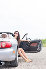 Young woman sitting in convertible on country road against clear sky