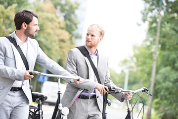 Businessmen looking at each other while holding bicycles outdoors