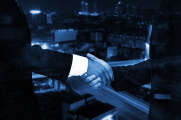 Double exposure of businessman handshake, business concept, successful business meeting on night city background, color tone effect.