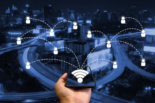 smart phone in hand and using internet wifi network connection communication technology concept on blurred night city background, color tone effect