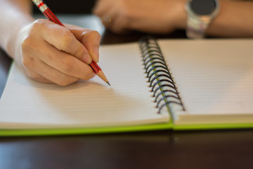 a woman working and holding red pencil and writing on notebook