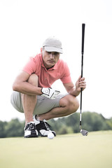 Obraz premium Middle-aged man aiming ball while crouching on golf course