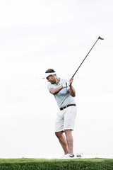 Full-length of mid-adult man swinging golf club against clear sky