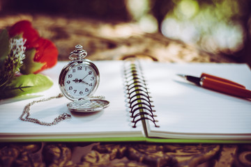 pen, packet watch and rose  on the desk, open a blank white notebook on table
