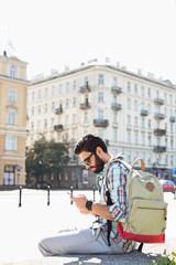 Side view of man with backpack using cell phone in city on sunny day