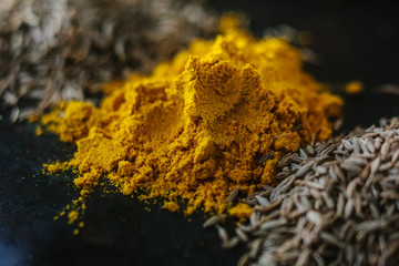 Turmeric powder spice on black, surrounded by other spices.