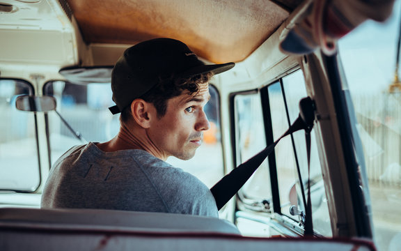 man sat in driving seat of a camper kombi van on a road trip
