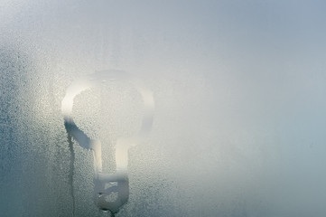 Lamp bulb symbol on sunny foggy window glass blurry condensation background, closeup image. Research and development scientific innovation