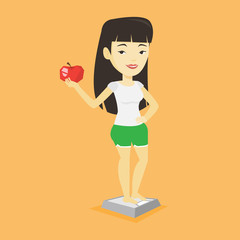Woman standing on scale and holding apple in hand.