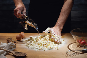 Cook hands kneading dough, adding water to flour. Low key shot, close up on hands, some ingredients around on table.