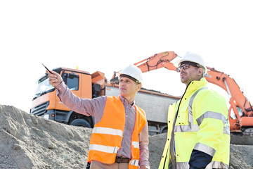 Engineer showing something to colleague while discussing at construction site against clear sky