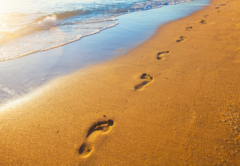 beach, wave and footprints at sunset time