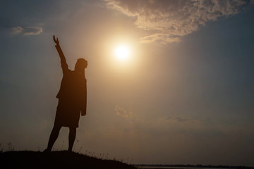 Silhouette woman with hands raised and sky with sunlight