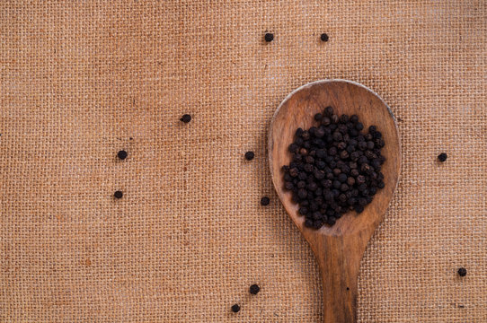 Top view to wooden spoon with black spicy pepper on burlap kitchen surface