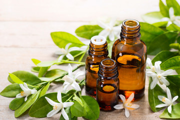 neroli essential oil in the brown glass bottle, with fresh white neroli flower and green leaves.